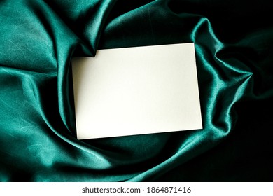 Mock up Greetings typing background Green color silk cloth, white paper Flat lay composition for greeting cards Season image Copy space