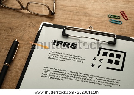 Mock IFRS document displayed on wooden desk with business accessories, featuring currency symbols and accounting standards information. Perfect for finance articles, compliance education content, and corporate blog illustrations.
