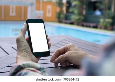 Mock Up Image Of Casual Man Hand Holding Black Mobile Phone With Blank White Screen On Table With Blurred Hotel Swimming Pool And Garden Background