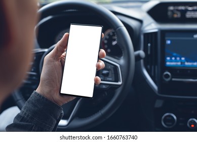 Mock Up Image Of Driver Hand Using Blank White Screen Mobile Smart Phone Inside A Car. Man Looking At Smartphone Screen Searching Location Via Gps Navigator Application, Close Up