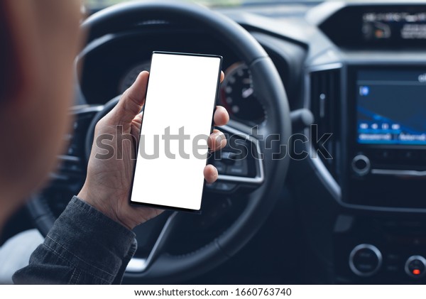 Mock up image of\
Driver hand using blank white screen mobile smart phone inside a\
car. Man looking at smartphone screen searching location via gps\
navigator application, close\
up