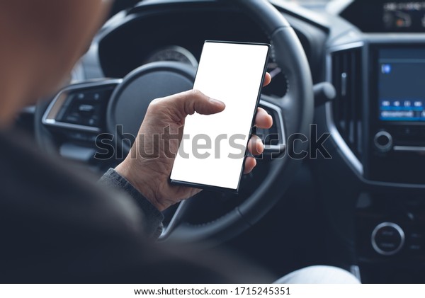 Mock up image of\
Driver hand using blank white screen mobile smart phone inside a\
car. Man touching on smartphone screen searching location via gps\
navigator application, close\
up
