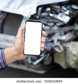 Mock Up For Insurance Service, Driving School, Tow Truck Call Or Web App Above Car Accident. White Mockup Screen Mobile Phone In Male Hands After Car Accident. Smartphone In Front Of Wrecked Car.