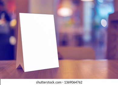 Mock Up Label The Blank Menu Frame In Bar Restaurant ,Stand For Booklets With White Sheets Paper Acrylic Tent Card On Wooden Table Cafeteria Blurred Background Can Inserting The Text Of The Customer.