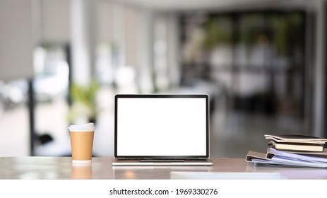 Mock up laptop computer, coffeecup and documents on white table in modern office. Blank screen for graphic display presentation montage.