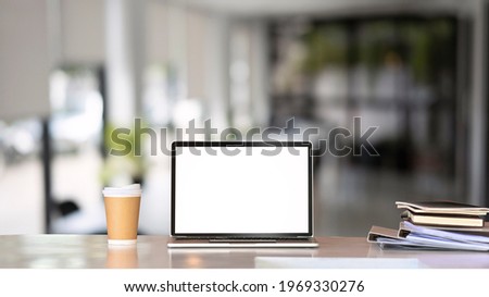 Mock up laptop computer, coffeecup and documents on white table in modern office. Blank screen for graphic display presentation montage.