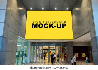 Mock up large billboard with clipping path on the wall over the entrance shopping mall, perspective yellow screen empty space to insert advertisement, blurred people walking in and out the door 
