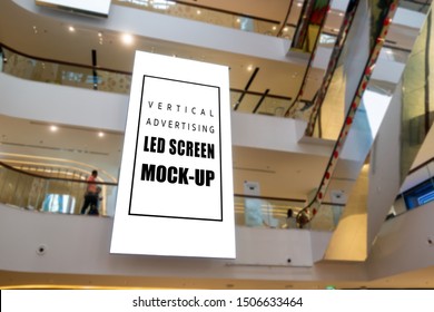 Mock up large blank vertical LED screen hanging from ceiling between floors near escalator with clipping path in shopping mall, empty space for insert media or information promotion