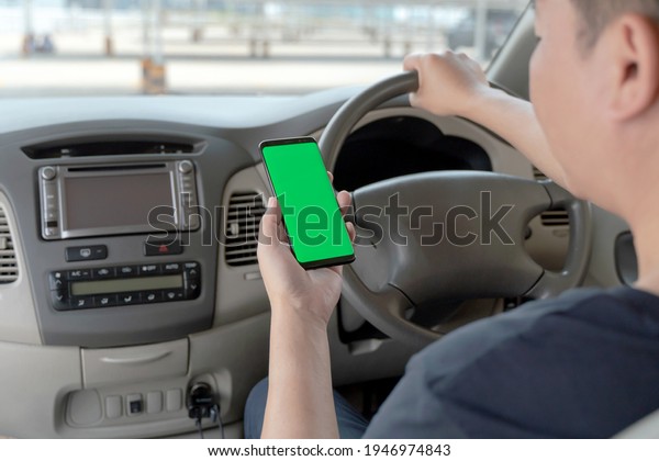 Mock up of man using mobile smart phone inside a car.
Driver hand holding blank green screen smartphone, searching
address and pin location via map navigator application,
transportation technology 