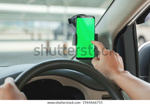 Mock up of man using mobile smart phone inside\
a car. Driver hand holding blank green screen smartphone, searching\
address and pin location via map navigator application,\
transportation technology