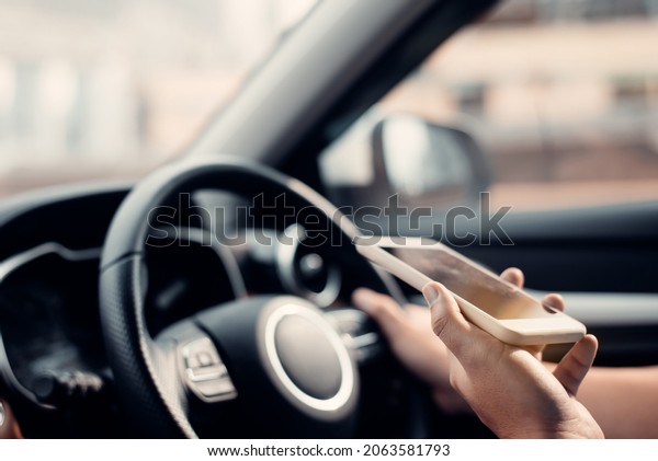 Mock up of man using mobile smart phone inside\
a car. Driver hand holding blank black screen smartphone, searching\
address and pin location via map navigator application,\
transportation technology