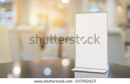 Mock up Menu frame  in Bar restaurant ,Stand for booklets with white sheets of paper acrylic tent card on wooden table on cafeteria  blurred background 