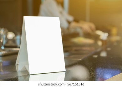 Mock up Menu frame on Table in Bar restaurant ,Stand for booklets with white sheets of paper acrylic tent card on cafeteria blurred ,Chef cooking in background.  - Shutterstock ID 567151516