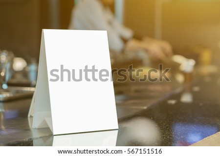 Mock up Menu frame on Table in Bar restaurant ,Stand for booklets with white sheets of paper acrylic tent card on cafeteria blurred ,Chef cooking in background. 