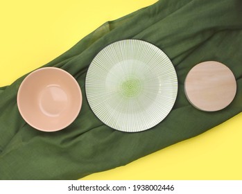 Mock up row of ceramic table ware with green fabric on yellow background. Minimalist summer kitchen setting. Eco friendly style. Trendy color design. Top view. Flat lay.