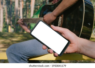 Mock up of a smartphone in front of a man playing the guitar. Against the background of the forest - Powered by Shutterstock