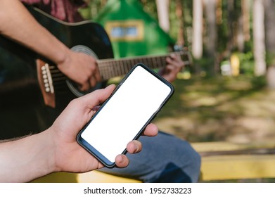 Mock up of a smartphone in front of a man playing the guitar. Against the background of the forest and houses in nature - Powered by Shutterstock