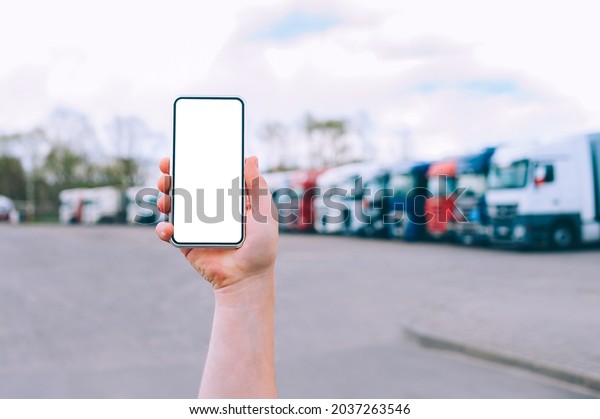 Mock up a smartphone in the\
hand of a man. Against the background of red trucks. Logistics\
concept