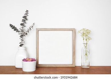 Mock up square wood frame with home decor.  Succulent, eucalyptus branches and flowers. Wooden shelf against a white wall. Copy space.