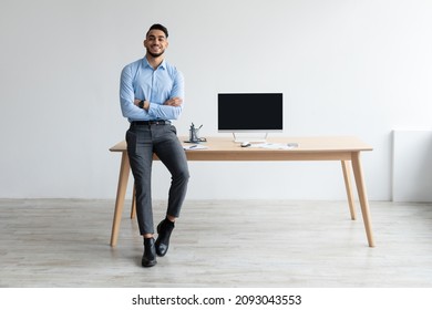 Mock Up Template. Happy Smiling Arab Man Sitting On Desk Posing With Folded Arms Showing Pc Computer With Blank Black Screen At Home Office, Free Copy Space. People, Technology, Remote Work Concept