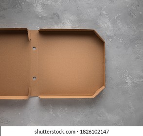 Mock Up Or Template With Partly Visible New Clean Brown Opened Empty Pizza Box Made Of Paperboard On Gray Stone Textured Table Surface. Large Copy Space. Home Delivery And Stay Home Concept.