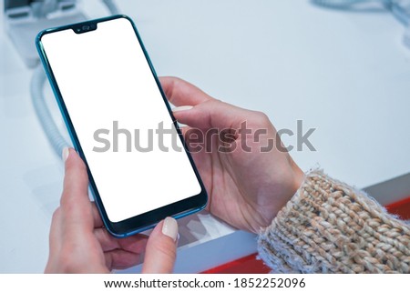 Mock up, copyspace, white screen, template, technology concept. Woman customer testing new model of smartphone with blank white display at electronic shop, store, trade show, exhibition: mockup image