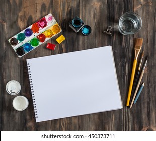 Mock up. Creative space. Artistic work tools on dark wooden table: watercolor, paintbrushes and water.
 - Powered by Shutterstock