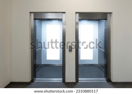 Mock up. Two empty elevators with opened metallic cabins doors and vertical poster media template frames hanging on cabin wall inside