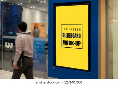 Mock up vertical blank yellow screen LED billboard or signboard in blue frame with clipping path near entrance modern shop, blurred man walking on passage, empty space for advertising or information
