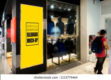 Mock Up Vertical Signboard At The Wall With Clipping Path, Blank Yellow Screen For Advertising Or Information Indoor Billboard Front Of Clothing Store With Blurred People Walking Pass