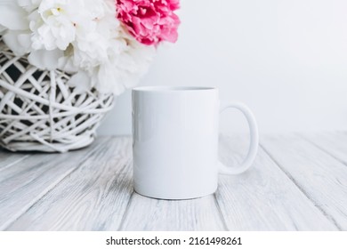 Mock up of white blank coffee mug perfect for your own design or quote with peony flowers on background. Copy space.