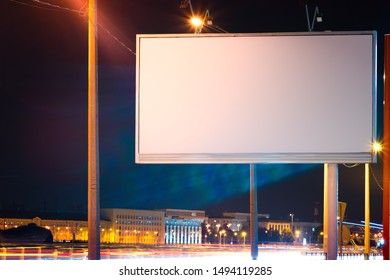 A mockup of a billboard at the edge of the road, with a line of light from cars. lit by lanterns for advertising at night in the city - Powered by Shutterstock