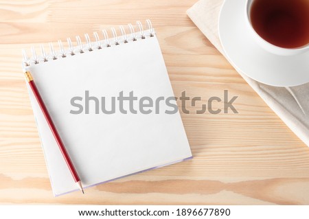 Mockup Blank notepad with pen, notebook and tea cup on wooden table. Top view notebook with blank pages Cup of Tea and red pencil on Light Wooden Background. Still life, business, or education