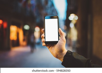 Mockup Of Blank Screen Of Smartphone, Male Hand Holding Modern Black Cellphone With Template Screen With Area For Your Logo Or Design, Evening City Street In The Background