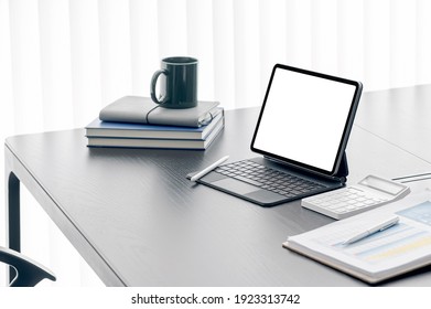 Mockup Blank Screen Tablet With Magic Keyboard And Supplies On Wooden Table In Modern Room.