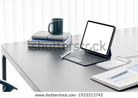 Mockup blank screen tablet with magic keyboard and supplies on wooden table in modern room.