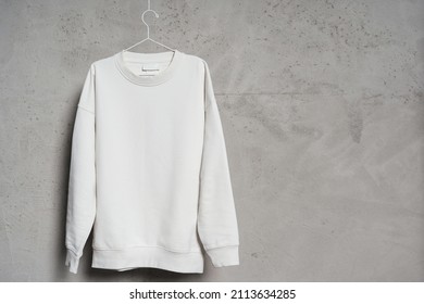 Mockup of blank white sweatshirt hanging on the thin metallic hanger against a concrete wall