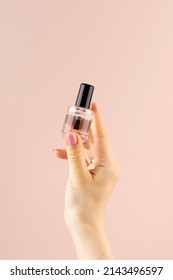 A mockup of a bottle with transparent nail polish in a woman's hand on a pink background. Manicure concept.