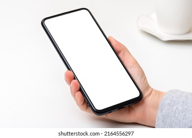 Mockup Cellphone. Female Hand With Cell Phone With Blank White Screen On White Table Background. Woman Hand Holding Black Cell Phone Smartphone With Blank White Screen