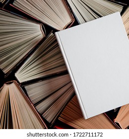 Mockup Of Closed Blank Square Book Rests On Open Old Multicolored Books