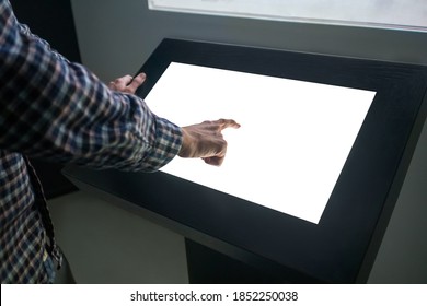 Mockup Closeup Image: Man Hand Touching White Empty Interactive Touchscreen Display Kiosk In Dark Room Of Technology Museum. Mock Up, Template, Scifi, Education, Futuristic And Technology Concept