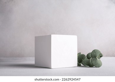 Mockup for cosmetic or other product. White cube pedestal with green eucalyptus branch on grey background - Shutterstock ID 2262924547