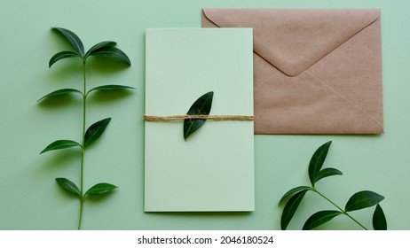 Mockup Of Craft Paper Envelope With Blank Green Card On Light Green Background With Plants Leaves Close-up. Wedding, Happy Birthday, Valentine's Day, Mother's Day Greeting, Invitation Card Concept.