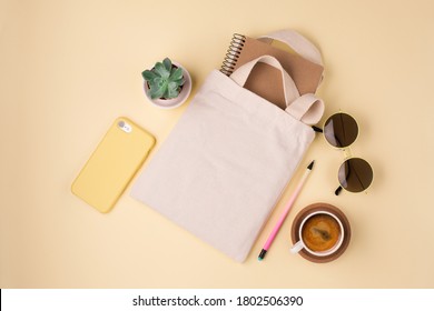 Mockup design bag concept. Top view of blank white tote bag canvas fabric with sunglasses and cup of coffee. Cloth shopping sack mockup with copy space. Yellow background.