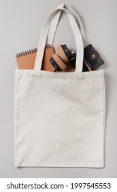 Mockup empty template White cream shopping bag for your design, eco friendly, zero waste with copy space. Minimalism flat lay. Inside there are headphones, a notebook and a men's wallet.