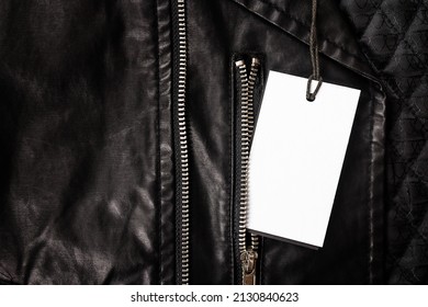 Mockup - an empty white label for text on a drawstring lies on a black leather jacket with a metal zipper. Close-up, T-shirt template design, print presentation layout. Flat lay, top view.