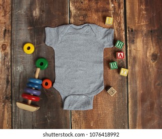 Mockup Flat Lay Of Gray Baby Bodysuit Shirt On Rustic Wood Background With Wooden Blocks And Baby Toys