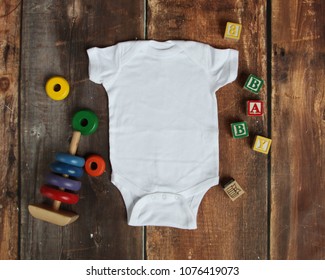 Mockup Flat Lay Of White Baby Bodysuit Shirt On Rustic Wood Background With Wooden Blocks And Baby Toys