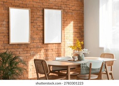 Mockup frames on brick wall in bright modern dining room interior with wooden table, woven chairs, flower vase, houseplant and sunlit window