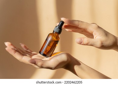 Mockup of glass bottle with dropper lid in female hands. Amber-colored container with cosmetic product, serum on brown background in rays of sunlight. Concept of beauty - Shutterstock ID 2202462205